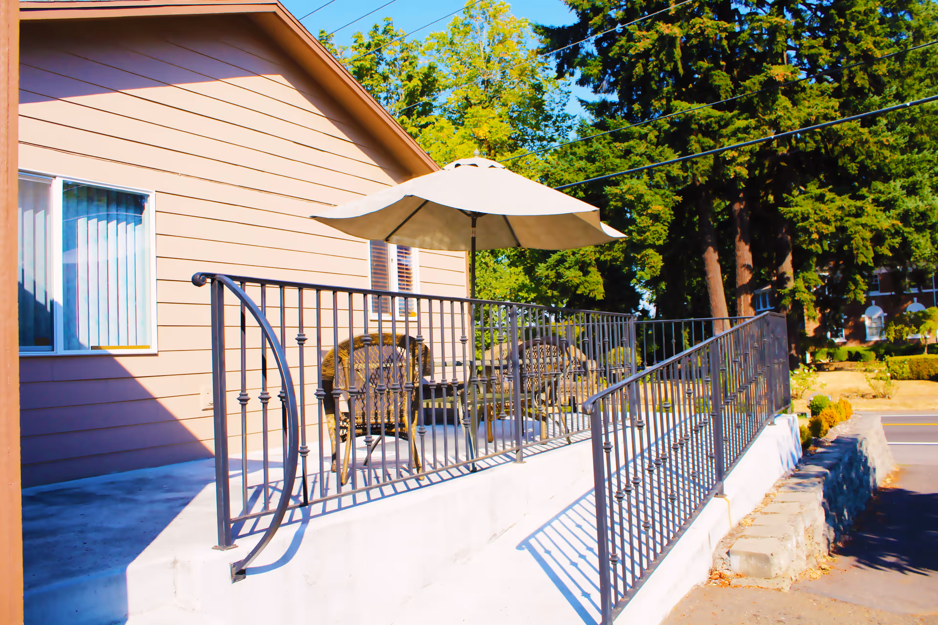 A front patio with metal railing, wicker chairs and a large umbrella next to a light-colored building.