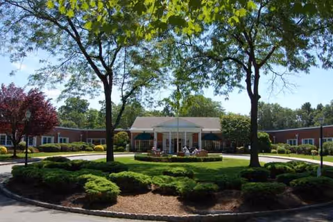 A circular driveway and landscaped greenery frame the front entrance of a senior living center.