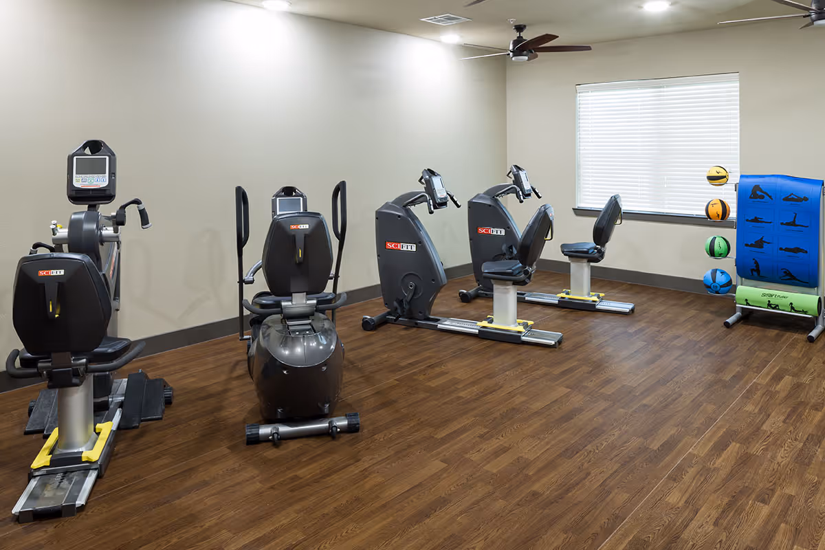 A well-lit exercise room with several recumbent stationary bikes and a rack of fitness balls and mats.