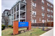 Exterior view of a multi-story brick senior living building with balconies and a blue Golden Livingcenter sign on a brick pedestal by the sidewalk.