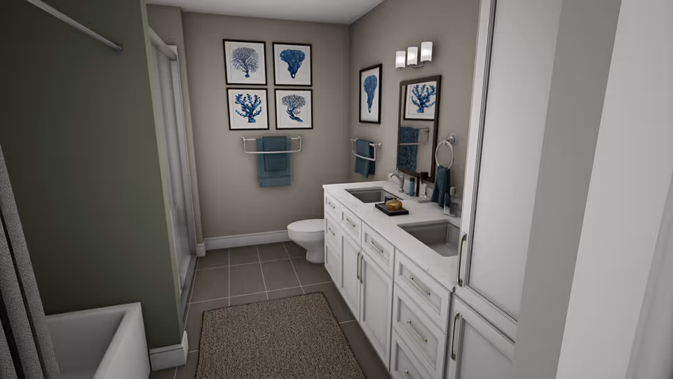 A modern bathroom with a double sink vanity featuring white cabinets and a marble countertop. There is a large mirror above the sinks with a light fixture. On the wall opposite the sinks, there are four framed blue coral prints and a towel rack with a blue towel. The bathroom also includes a toilet and a shower with a glass door. The floor is tiled in gray, and there is a beige rug in front of the vanity.
