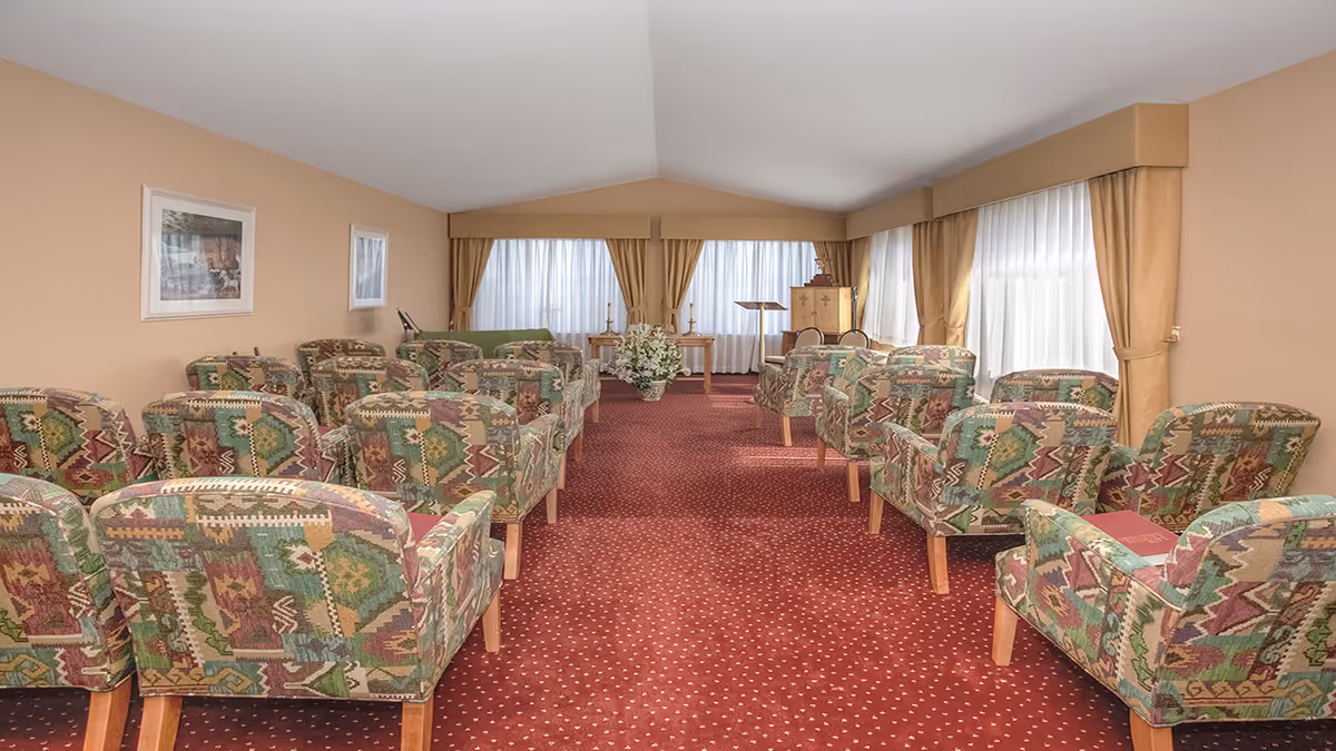 Carpeted interior meeting room with rows of patterned armchairs facing a small podium and curtained windows.