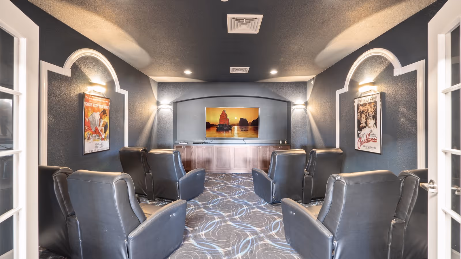 Small theater-style media room with black leather recliners facing a wall-mounted TV and framed movie posters.