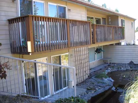 Two-story building exterior with wooden balconies and a small pond.