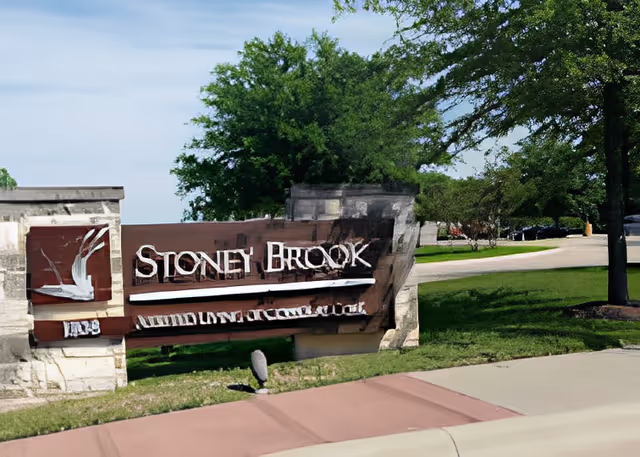 Stone Brook of Copperas Cove facility entrance sign made of stone and wood with trees and a driveway in the background.