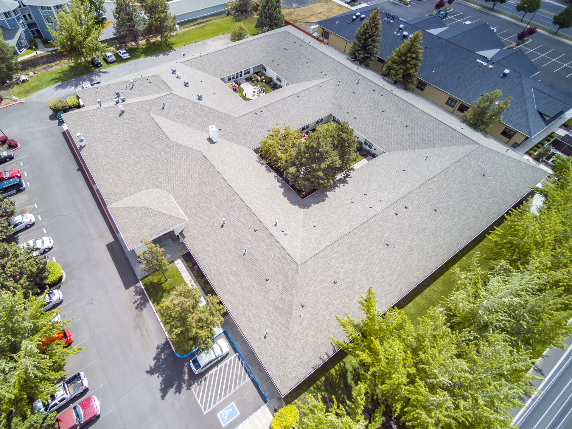 Aerial view of a single-story assisted living building arranged around a central courtyard, with surrounding parking lot and trees.