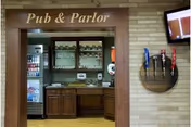 Interior view of a small pub area labeled 'Pub & Parlor' with a service counter, cabinets, a beverage fridge, glass shelves, drink taps on the wall, and a TV.