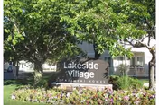 Entrance sign reading 'Lakeside Village' surrounded by trees and flowers in front of an apartment building.