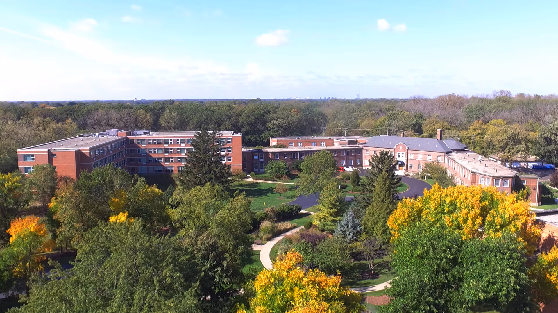 Aerial view of a red-brick senior living campus surrounded by trees and winding paths in autumn.