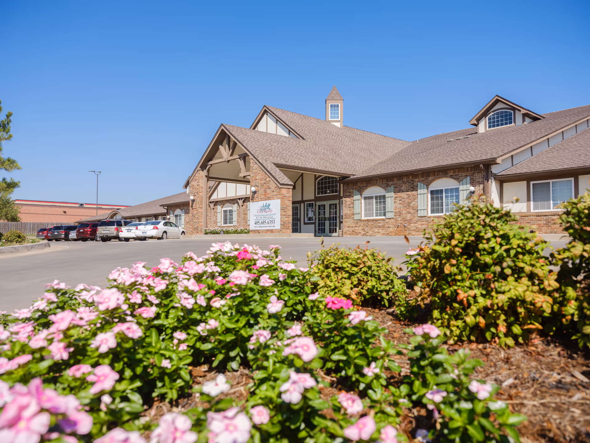 Front view of Village at Oakwood facility with brick facade and blooming flowers in foreground.