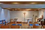 Small chapel interior with rows of wooden chairs facing an altar and a crucifix on the wall.