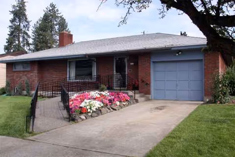 Red brick, single-story building with a blue garage door and flowering bed near entrance.