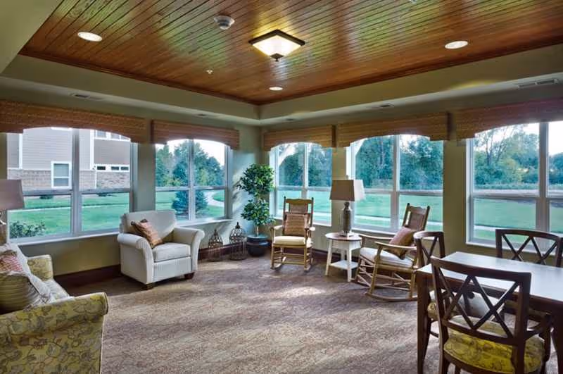Bright senior living lounge with cushioned seating, large windows, and a wooden ceiling.