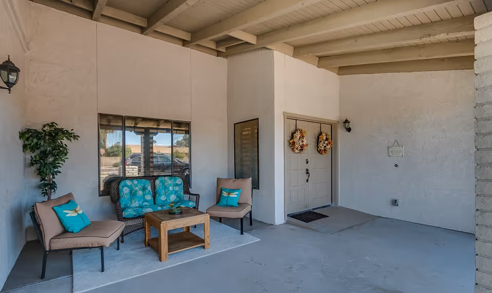 Covered front entryway with a seating area of chairs, a loveseat, a coffee table, and double doors decorated with wreaths.