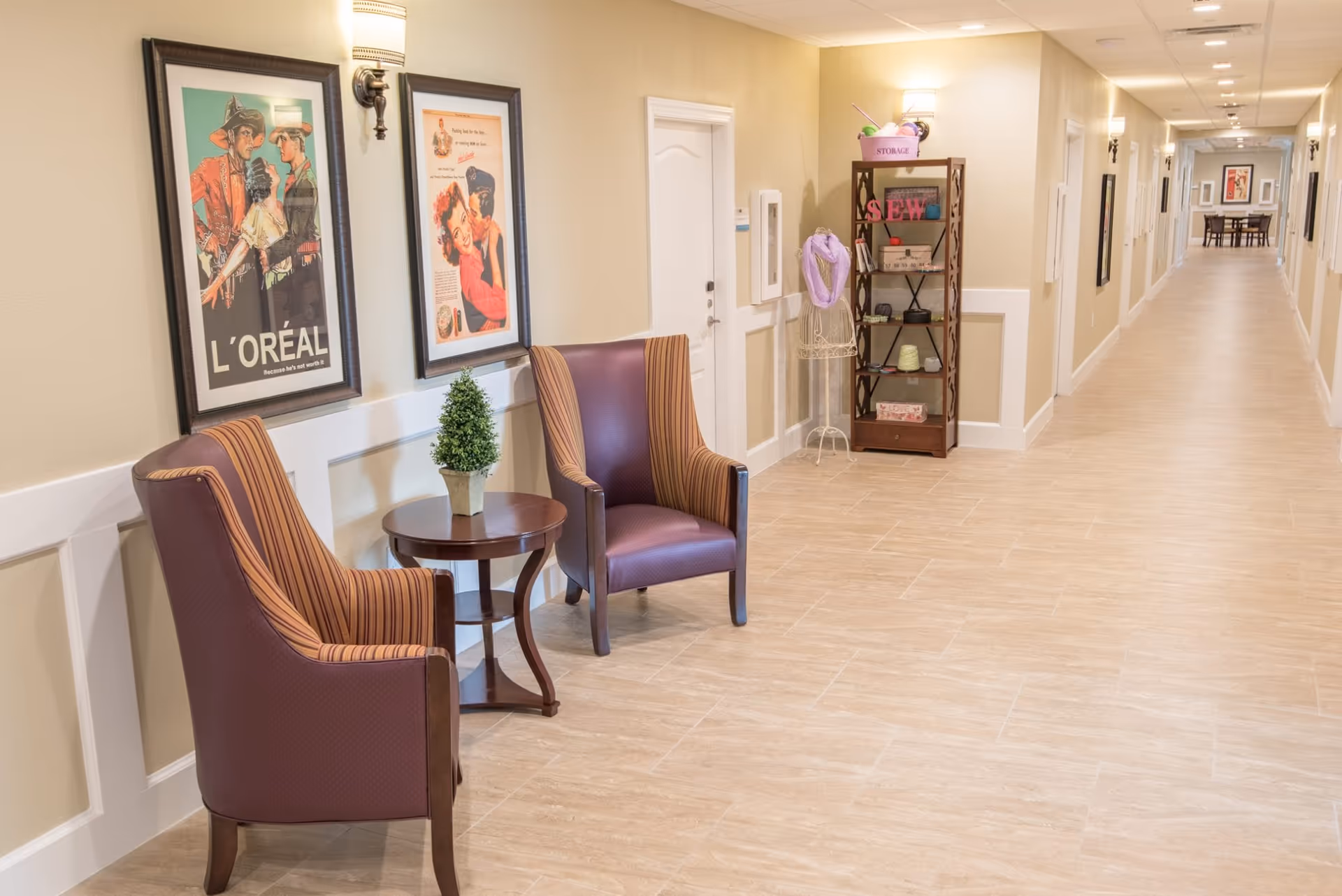 Well-lit interior hallway with two upholstered chairs and a small table beside framed posters and shelving.