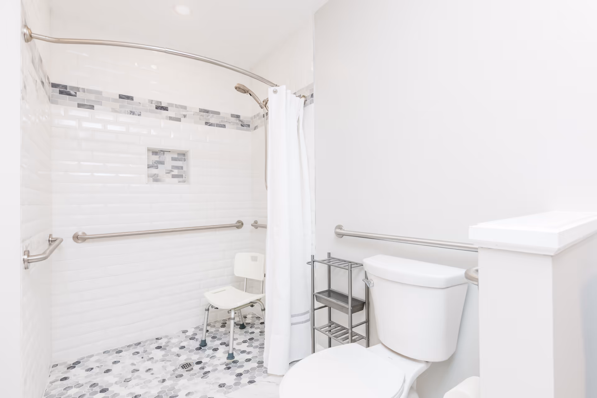 Bright accessible bathroom with a walk-in tiled shower, shower chair, grab bars, and a toilet.