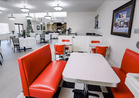 Communal dining room with red diner-style booths and tables, chandeliers, and a decorated Christmas tree in the background.