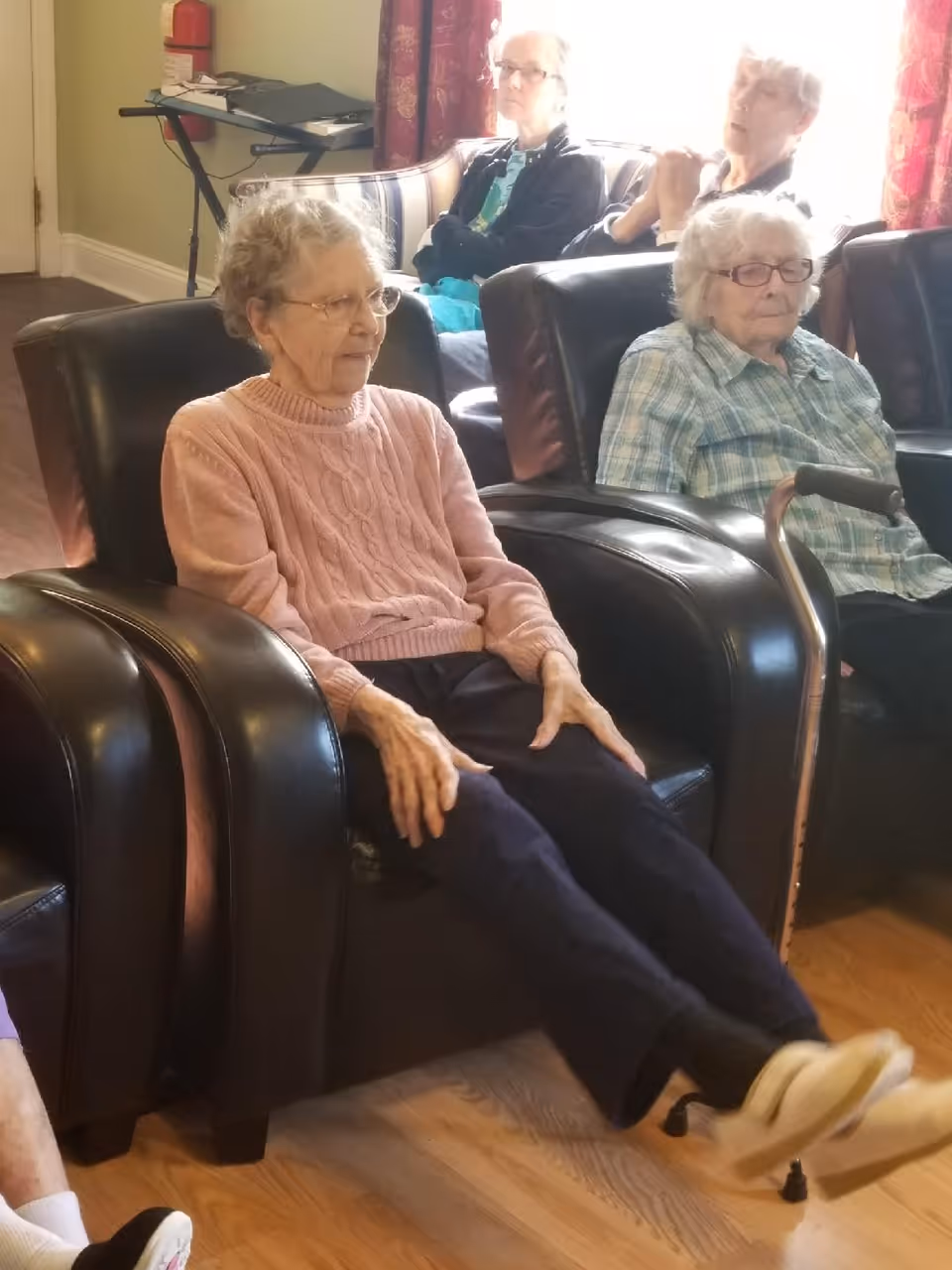 Several elderly women seated in leather recliners in a senior living facility common room.