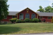 Red, single-story facility with large arched windows and manicured lawn in front.