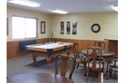 A recreation room with a pool table, round tables, and wooden chairs.
