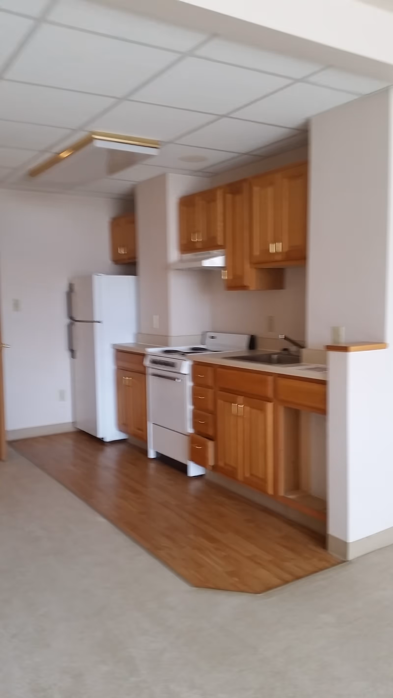 Compact kitchen area with wooden cabinets, a white refrigerator and stove, sink, and laminate flooring.
