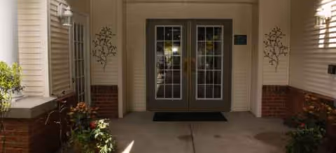 Double glass doors framed by brick and siding, with potted plants at a sheltered entrance.