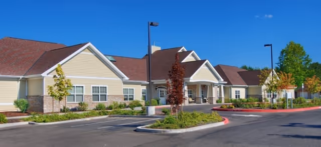 Single-story senior living campus with pastel exterior, parking, and landscaped entrance.