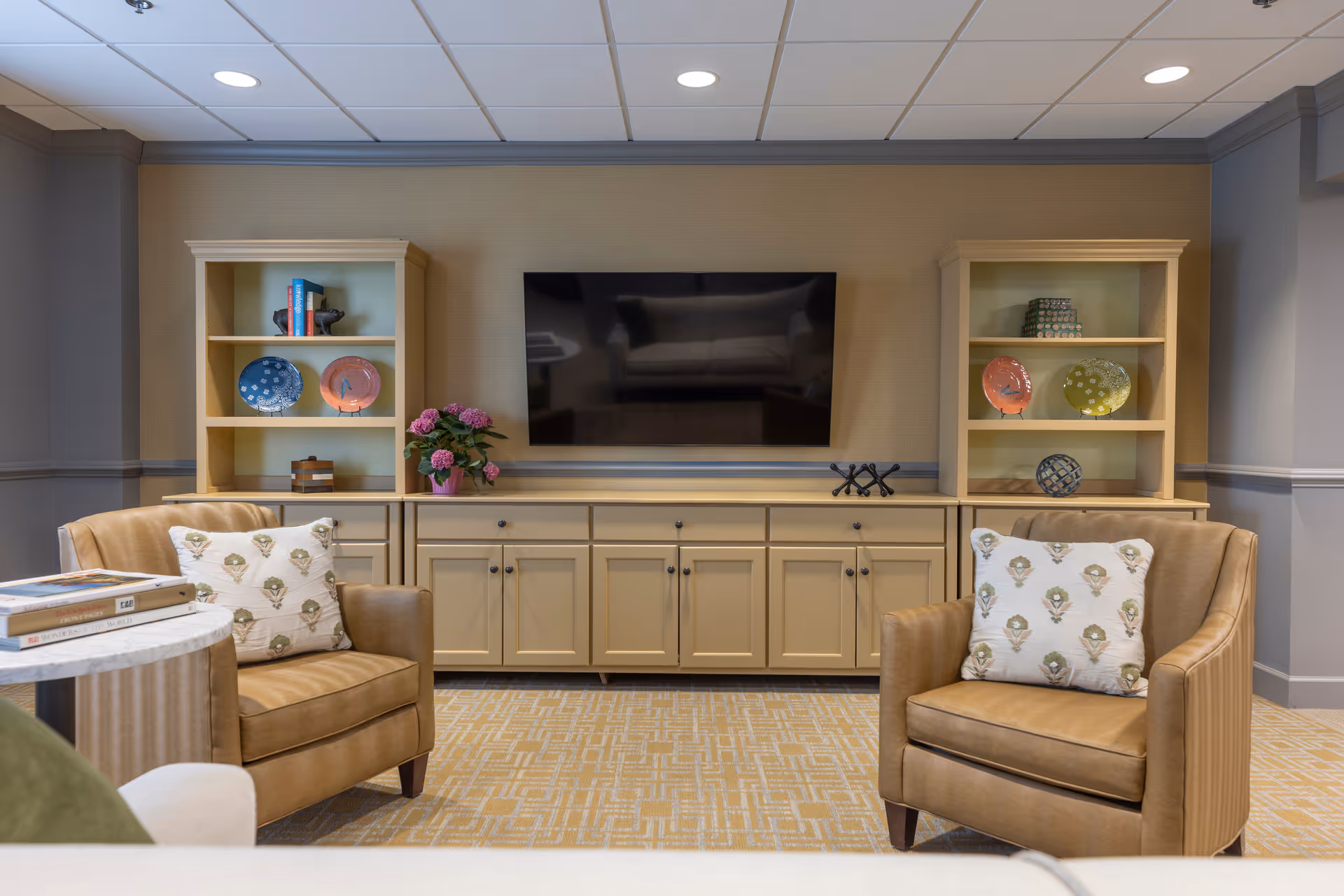 Cozy sitting area with two leather armchairs facing a wall-mounted TV flanked by built-in shelving and cabinets.