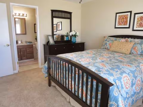 A furnished bedroom with dark wood bed, dresser, mirror, flowers, and framed art.