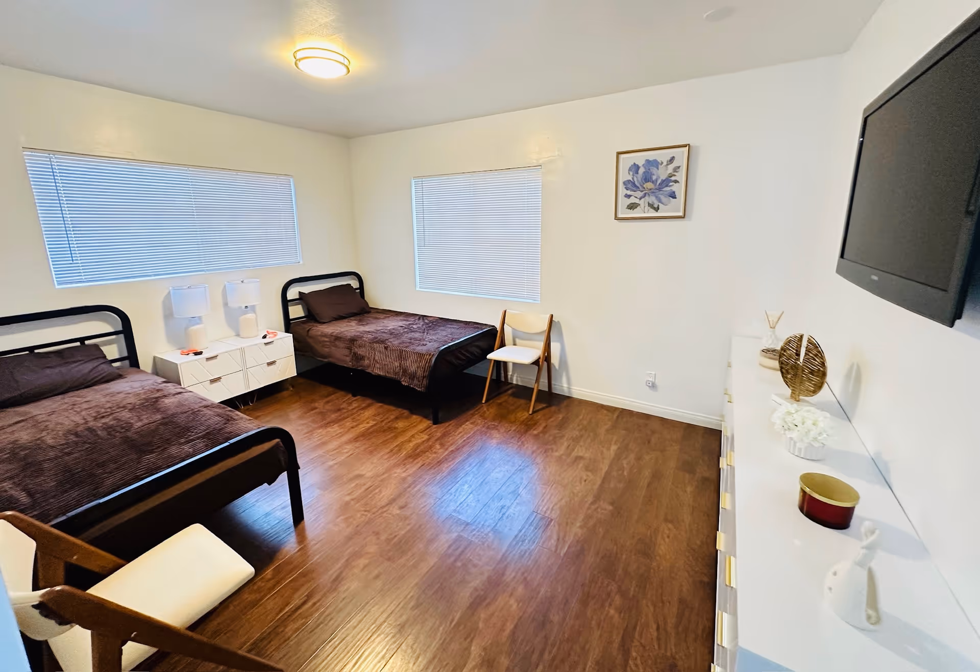 A two-bed senior living bedroom with two single beds, nightstands, dresser, and mounted TV.