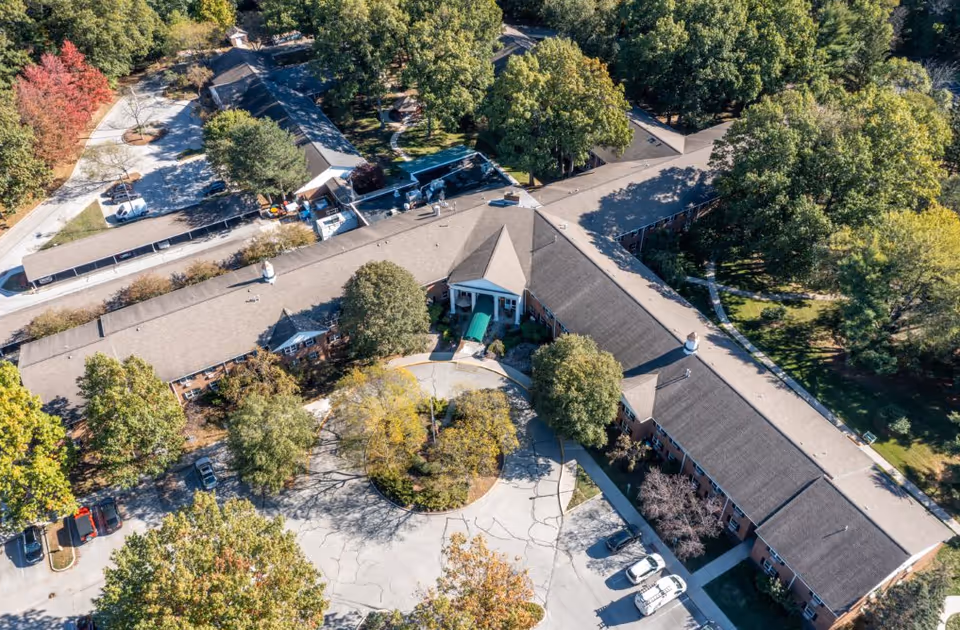Aerial view of a senior living campus with central entrance, wings, and tree-lined parking.