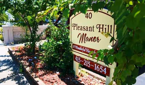 Outdoor sign reads Pleasant Hill Manor beside greenery and a walkway