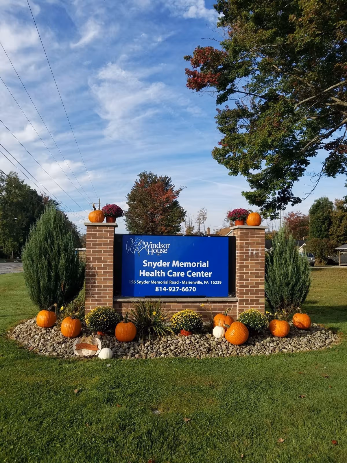 Brick entrance sign for Snyder Memorial Health Care Center decorated with pumpkins and plants on a grassy lawn under a blue sky.