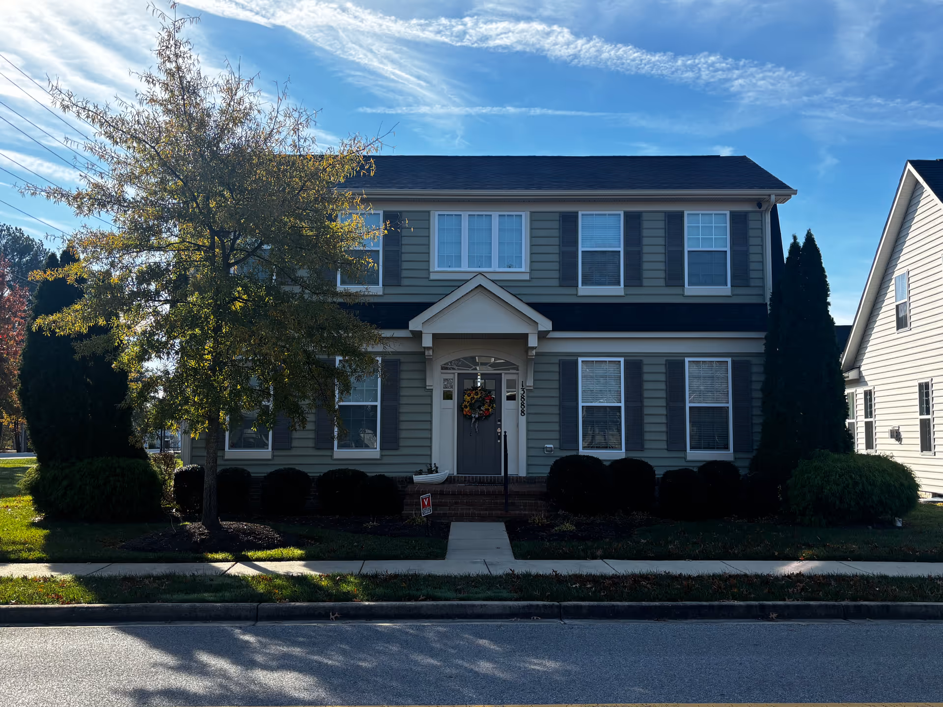 Front exterior of a two-story suburban house with a central entrance, shuttered windows, and a tree in the front yard.