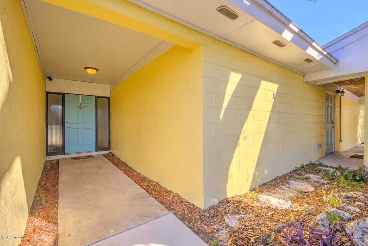 Exterior view of a yellow building with a covered walkway and blue entry doors.