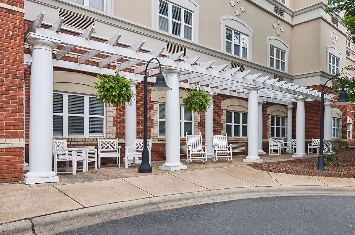 Exterior view of Summit Place of South Park featuring a covered entrance with white columns, hanging plants, and seating area.