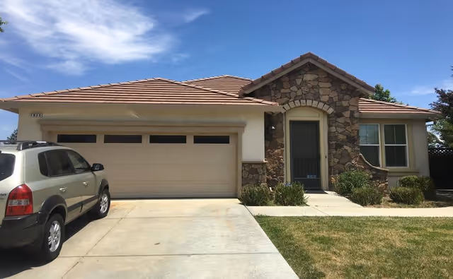 Single-story suburban home with a stone-accented facade, two-car garage, parked SUV, driveway, and front lawn under a blue sky.