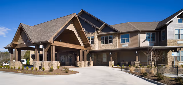 Exterior view of a senior living facility named Northshore Heights featuring a large covered entrance with wooden beams and stone pillars, a two-story building with multiple windows, and a clear blue sky above.
