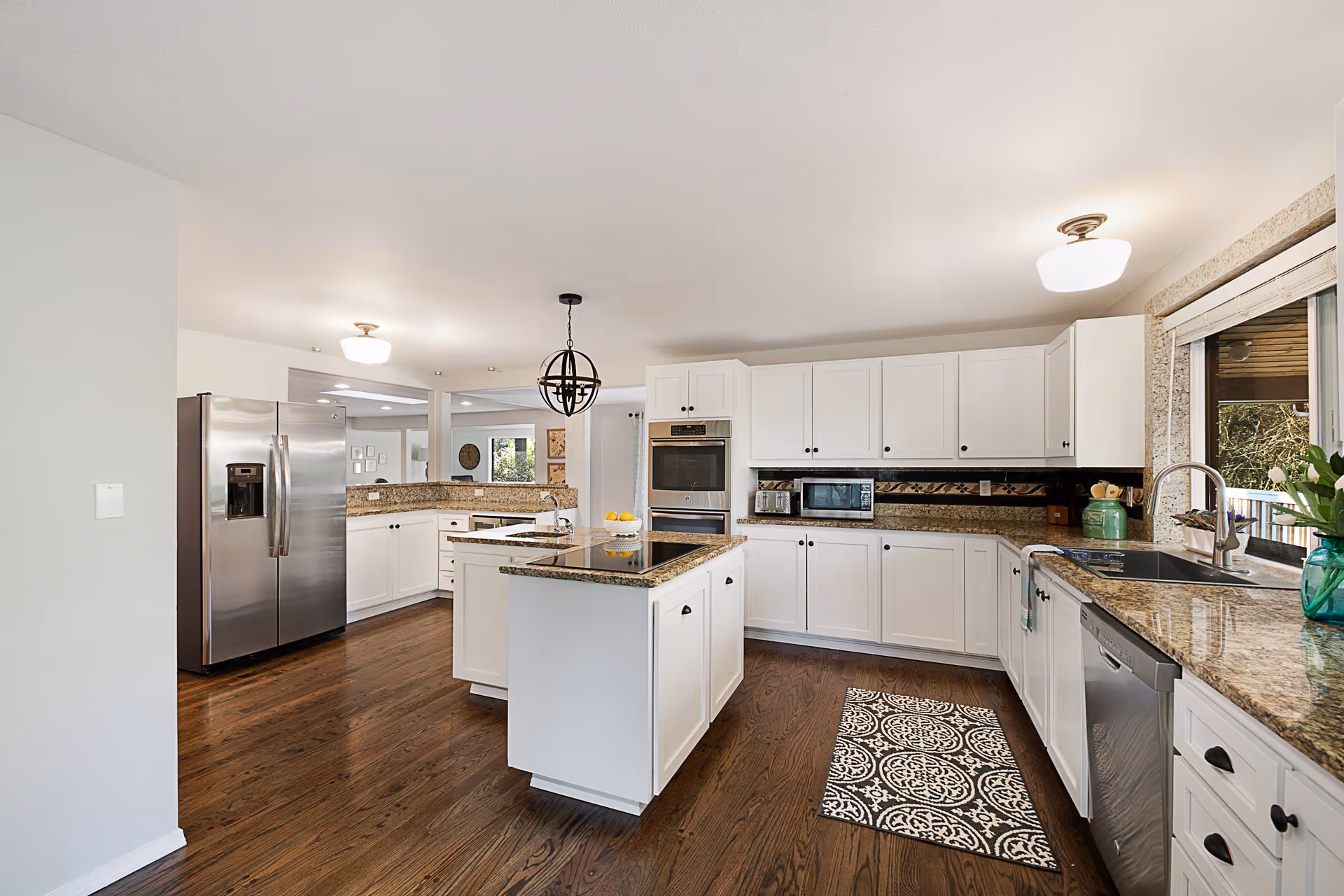 Bright modern kitchen with white cabinets, a central island, stainless steel appliances, and granite countertops.