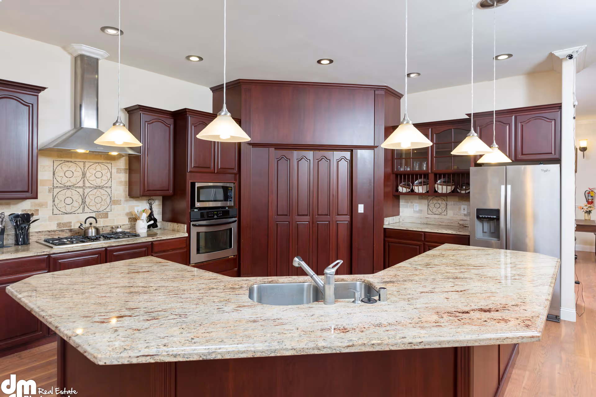 Spacious kitchen with a large granite island, dark wood cabinets, pendant lights, and stainless steel appliances.