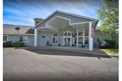 Front entrance of a senior living facility with a covered porte-cochere, American flag, and paved driveway.