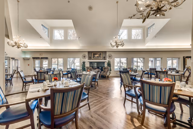 Spacious, well-lit dining room with multiple set tables, striped chairs, chandeliers, skylights and large windows.