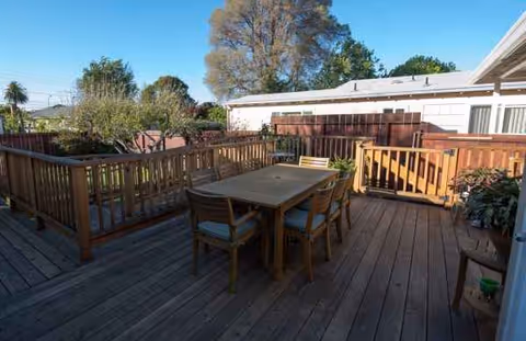 Outdoor wooden deck with a table and chairs, bordered by railings and trees.