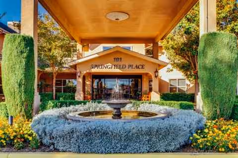 Front entrance of Springfield Place senior living with a circular fountain and manicured shrubs.