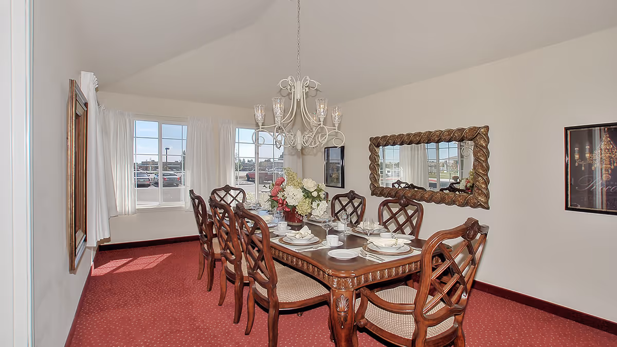 Formal dining room with a wooden table set for a meal, upholstered chairs, chandelier, and a large decorative mirror.
