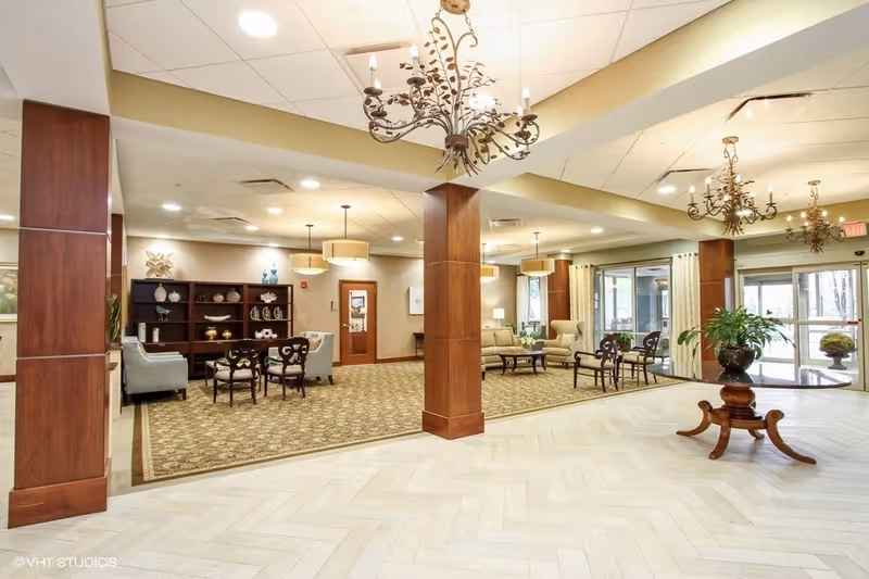Spacious lobby-style common area with seating, chandeliers, wooden columns, and large windows.