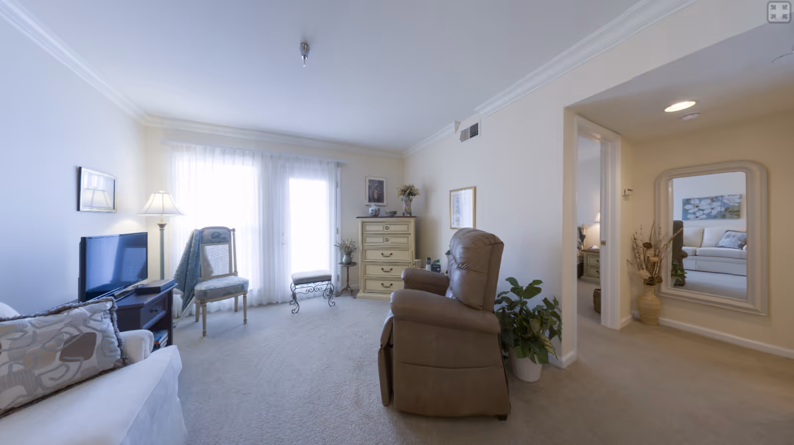 Bright living room with a recliner, sofa, chairs, TV, dresser, and sliding glass doors with sheer curtains.