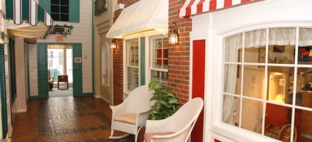 Indoor hallway styled like a small street with storefront facades, awnings, wicker chairs and a tiled floor.