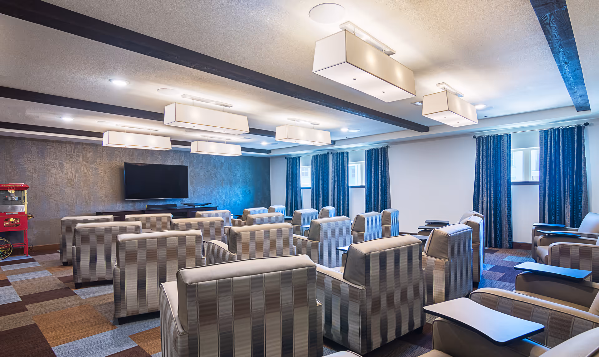 A comfortable media room with rows of upholstered armchairs facing a wall-mounted TV and a popcorn machine at the side.