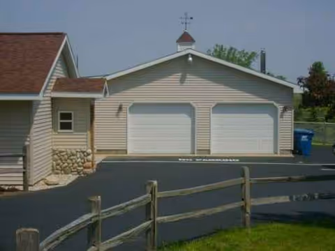 Beige, single-story building with two white garage doors; a wooden fence in foreground.